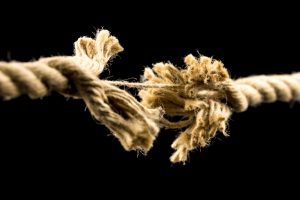 Closeup of frayed rope about to break. Isolated over black background.