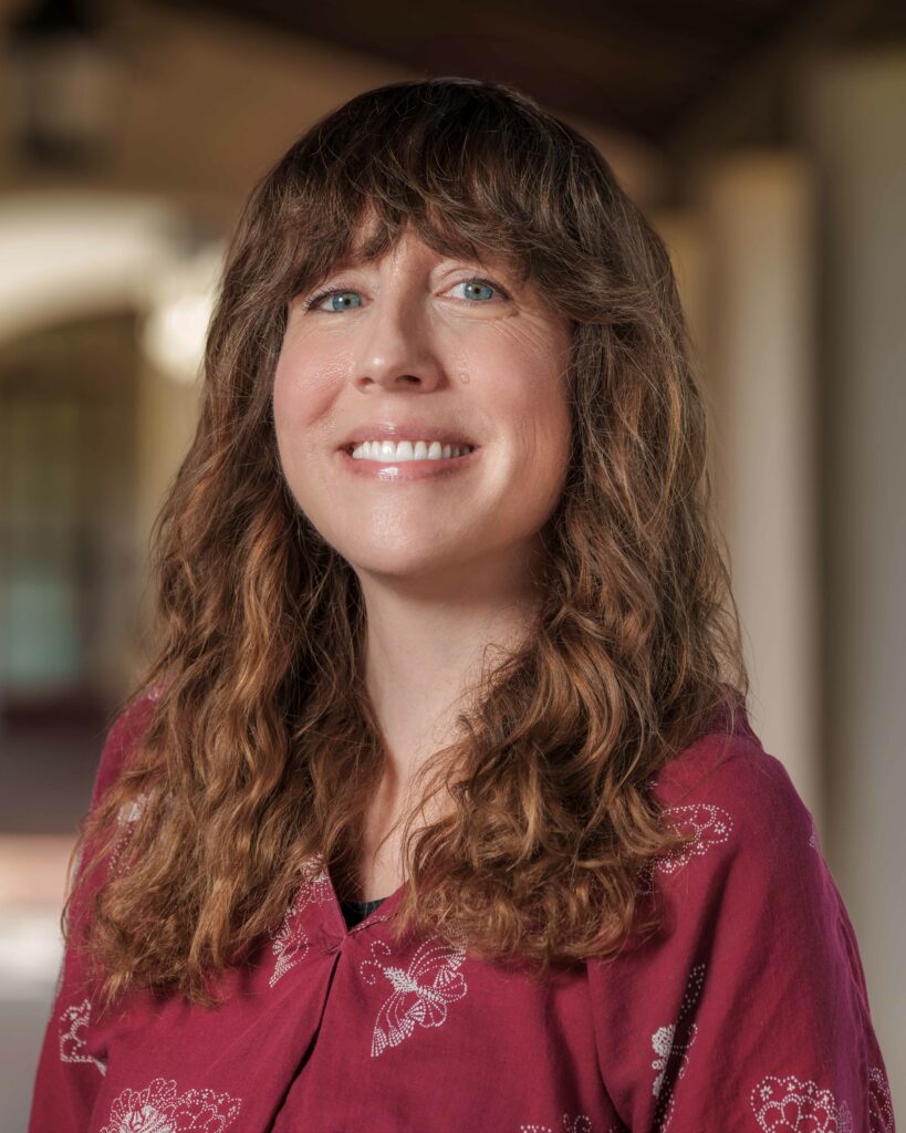 Stacey Beauregard is a white, female with wavy brown hair and blue eyes smiling towards the camera.