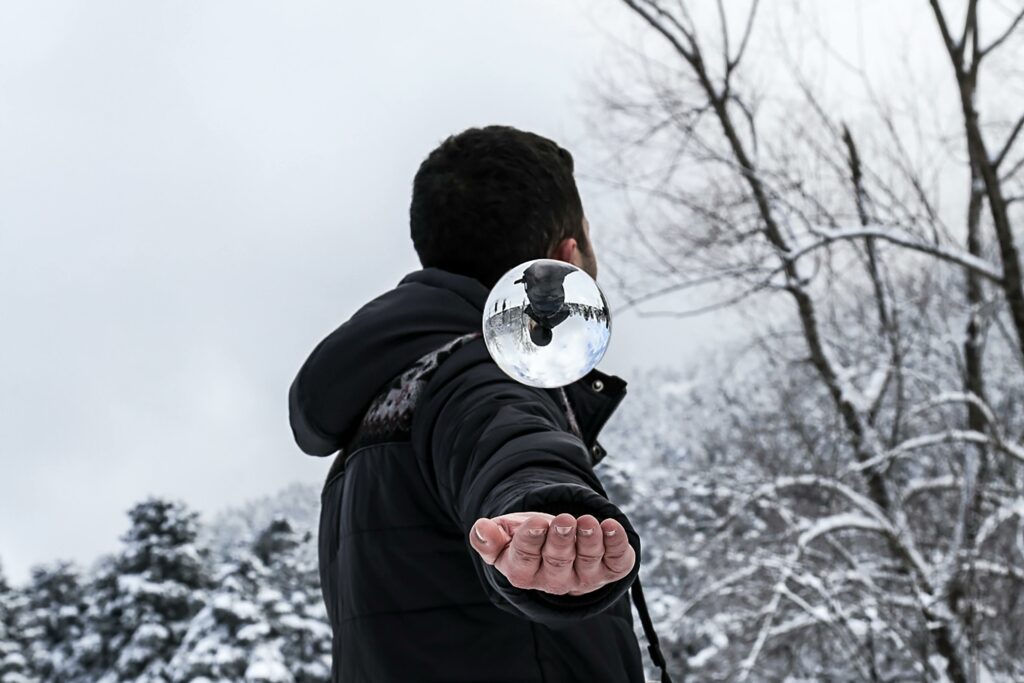 A person looking away wearing a Black Jacket in the snow with their palm out and a clear orb floating above 